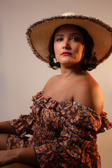 Beautiful and elegant brown skin woman wearing a straw hat and floral pattern dress. Ideal for vacations, summer, lifestyle. Studio portrait with copy space.
