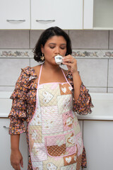 Beautiful woman in apron drinking a cup of coffee in home kitchen. Housewife enjoying a coffee break. Perfect for housework, domestic life, hot beverages.