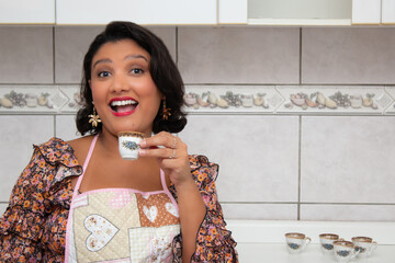 Cheerful woman in apron drinking a cup of coffee in home kitchen. Housewife enjoying a coffee break. Perfect for housework, domestic life, hot beverages.