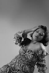 Attractive woman sitting on the ground, eyes closed, placing her hand in her hair. Feminine black and white dramatic portrait with copy space ideal for beauty, lifestyle, femininity.