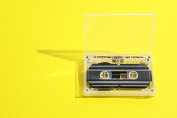 One audio cassette in open box on yellow background, above view. Space for text