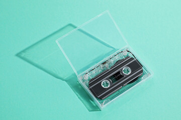 One audio cassette in open box on turquoise background, above view