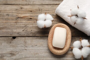 Soap bar, towel and cotton flowers on wooden table, flat lay. Space for text