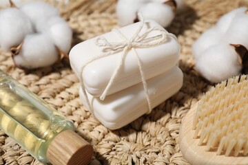 Soap bars, cotton flowers, cosmetic product and brush on wicker mat, closeup