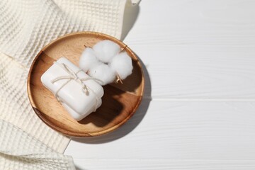 Soap bars, towel and cotton flower on white wooden table, above view. Space for text