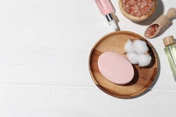 Soap bar, cosmetic products and cotton flower on white wooden table, flat lay. Space for text