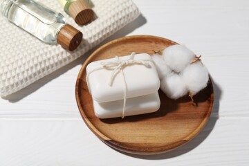 Soap bars, cosmetic products, towel and cotton flower on white wooden table, above view