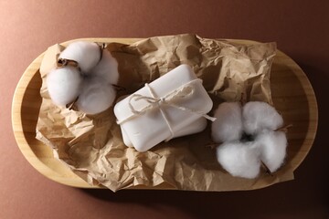 Soap bars and cotton flowers on brown background, top view