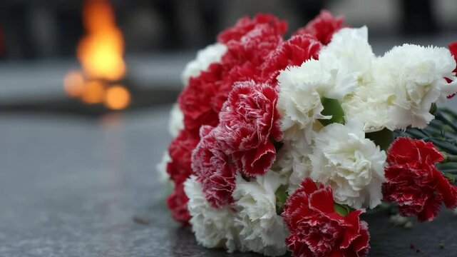 Red and white carnations on memorial ground with eternal flame background