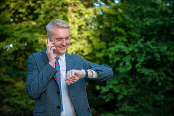 Businessman talking on smartphone and checking time on smartwatch outdoors.