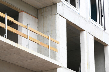 Modern concrete building with construction scaffold. Urban architecture in daylight. Structural facade with windows and safety railing. Unfinished exterior of multistory building.