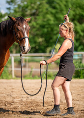 Woman is training horse on cord, holding it on leash. Horse moves in circle in an outdoor paddock....