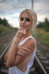 Obraz premium Portrait of a young beautiful blonde girl in a white blouse and summer hat on railway tracks.
