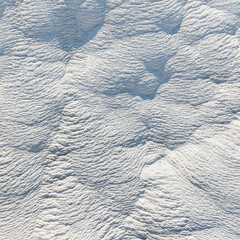 Close-up of natural travertine surface in Pamukkale, Türkiye, formed by calcium deposits from thermal spring waters. Bright sunlight highlights detailed textures and layered mineral formations.