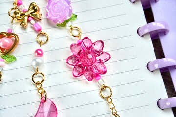 Close up pink flower glass beads isolated on horizontal gold chain bag charm decorations and note book lined paper background.