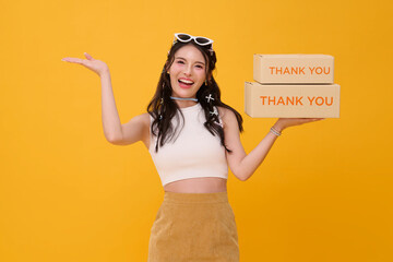 Happy beautiful Asian woman smiling holding package parcel box mockup and open hand welcome isolated on yellow background. parcel post