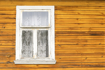Old rustic white wooden window on yellow timber wall. Traditional rural architecture detail. Weathered frame and lace curtain. Countryside house style with natural wood texture.