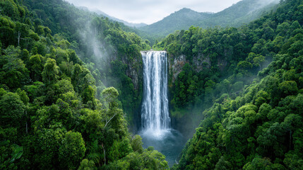 Wide shot of powerful waterfall surrounded by lush green forest and mist in mountainous landscape creating serene atmosphere