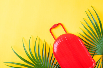 Red suitcase and palm leaves the yellow background. Travel and summer vacations concept. Mockup with copy space. Flat lay