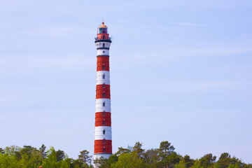 Striped lighthouse rising above greenery by the Gulf of Finland, calm coastal scene with symbol of guidance and safety on the shore
