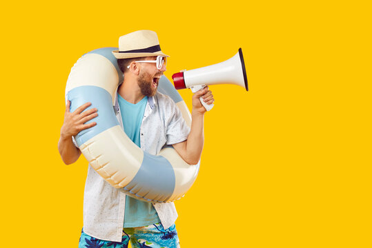 Funny, crazy man in summer clothes, sunglasses, sun hat and beach ring standing isolated on yellow background, making holiday sale announcement and shouting loudly in megaphone voice volume amplifier