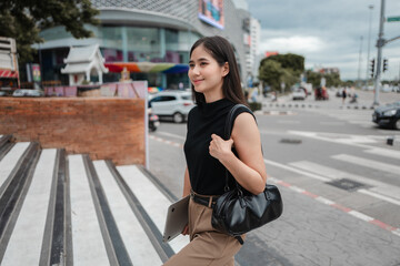 Young Asian office worker walking in the city carrying laptop and handbag