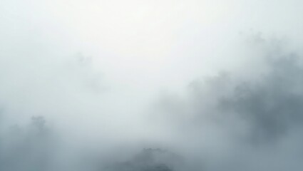 Misty mountain peaks emerge from thick fog with a bright sky above creating an ethereal and atmospheric landscape scene