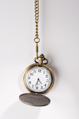 Bronze vintage round clock with hands and numbers on a chain hanging on a white background
