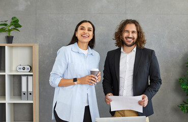 Portrait of two smiling business people man and woman standing in office near workplace and looking...