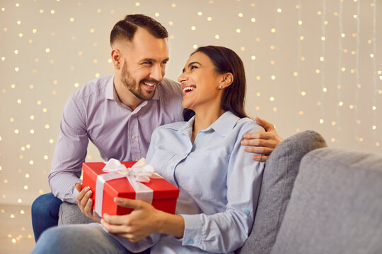 Delightful moment unfolds as a happy couple shares love and surprises on the sofa. The husband presents a gift box to wife, creating an atmosphere of joy, love, and togetherness at home.