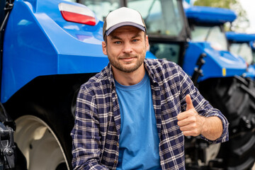 Portrait of modern farmer smiling and showing thumbs up with machinery in background