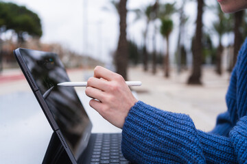 Student using tablet and stylus for online education in a park