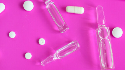 Transparent medical ampoules and white pills are arranged on a vibrant pink background, creating a...