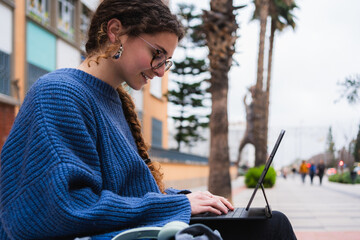 Young woman using tablet with keyboard, sitting on bench on university campus, studying outdoors