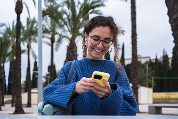 Young woman using mobile phone and smiling in a city park