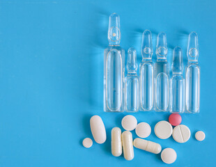 Transparent ampoules and white pills, along with one pink one, are arranged on a bright blue...