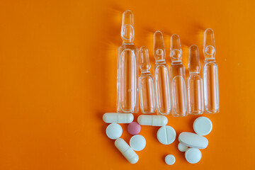 Transparent ampoules and white pills, along with one pink one, are arranged on a bright orange...