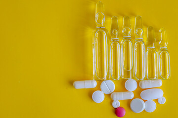 Transparent ampoules and white pills, along with one pink one, are arranged on a bright yellow...
