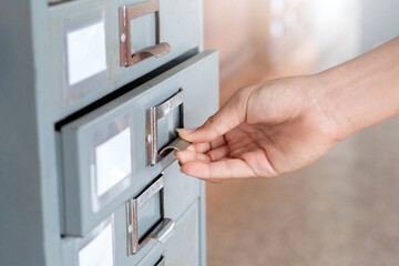 Hand pulling a drawer of an old metal filing cabinet in an archive or library, symbolizing search, organization, and vintage data storage.