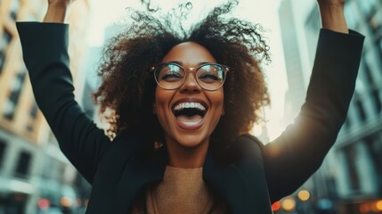 A stylish woman with curly hair and glasses joyfully raises her arms in the bustling city, symbolizing empowerment and success amidst the urban landscape as the sun sets behind her.
