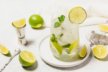 A refreshing drink served in a clear glass filled with ice cubes, lime slices, and fresh mint,...