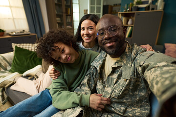 Portrait of Black middle aged man in military uniform sitting on sofa with smiling Caucasian woman...