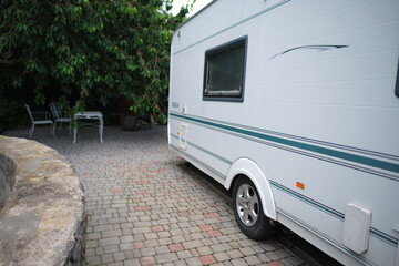 A white camper trailer is parked on a paved backyard near a brick house and cherry tree. RV travel...
