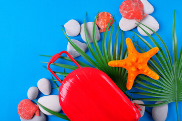 Travel flat lay with red suitcase, stones, starfish, sea shell and palm leaves on blue background. Summer vacations concept. Copy space