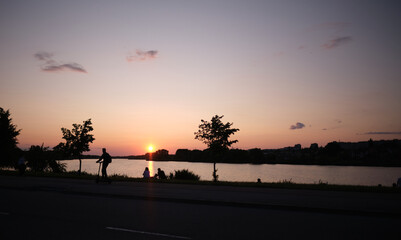 People near the lake against the backdrop of sunset over the city