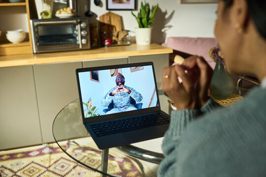 Caucasian woman sitting at glass table video calling Black middle aged man in military uniform on laptop, both making heart gesture with hands, kitchen background visible - Powered by Adobe