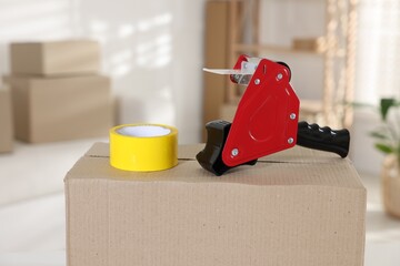 Dispenser with adhesive tape on cardboard box indoors, closeup