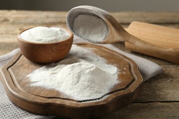 Wheat flour, spoon and rolling pin on wooden table, closeup