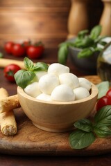 Tasty mozzarella cheese balls, breadsticks, tomatoes and basil on wooden table, closeup