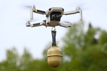 Small Flying unmanned aerial vehicle in flight mode with camera with a grenade attached outdoor on green forest background